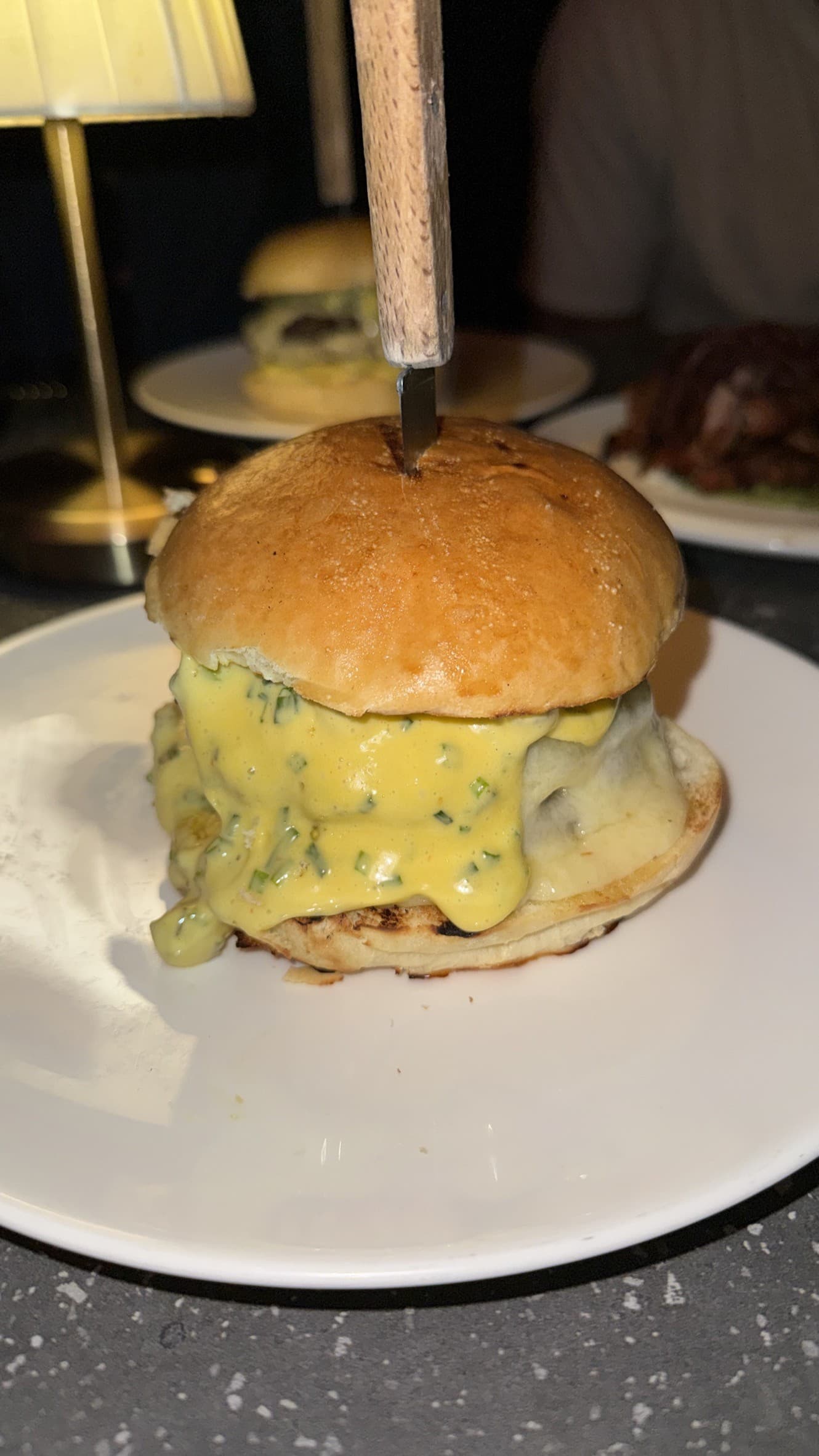 The Ella Burger at Ella Funt, covered in a yellow herb-flecked sauce, with a knife driven through the domed bun