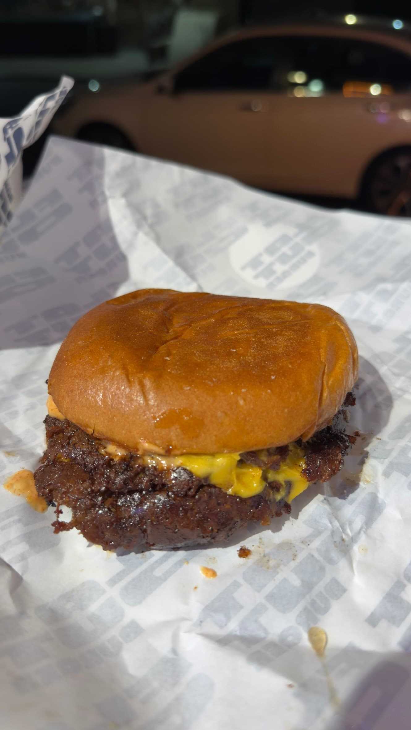 A Flat Out Burger double on the shop's branded paper: two lacy, deeply browned smashed patties with melted American cheese and orange sauce under a glossy brioche bun