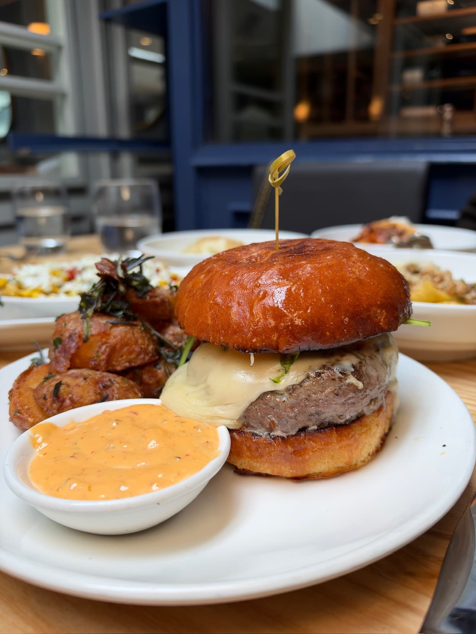 L'Artusi's L'Burger at lunch: a thick patty with melted pale cheese and arugula under a glossy toasted bun, with a pot of orange aioli on the side and crisp potatoes with fried herbs