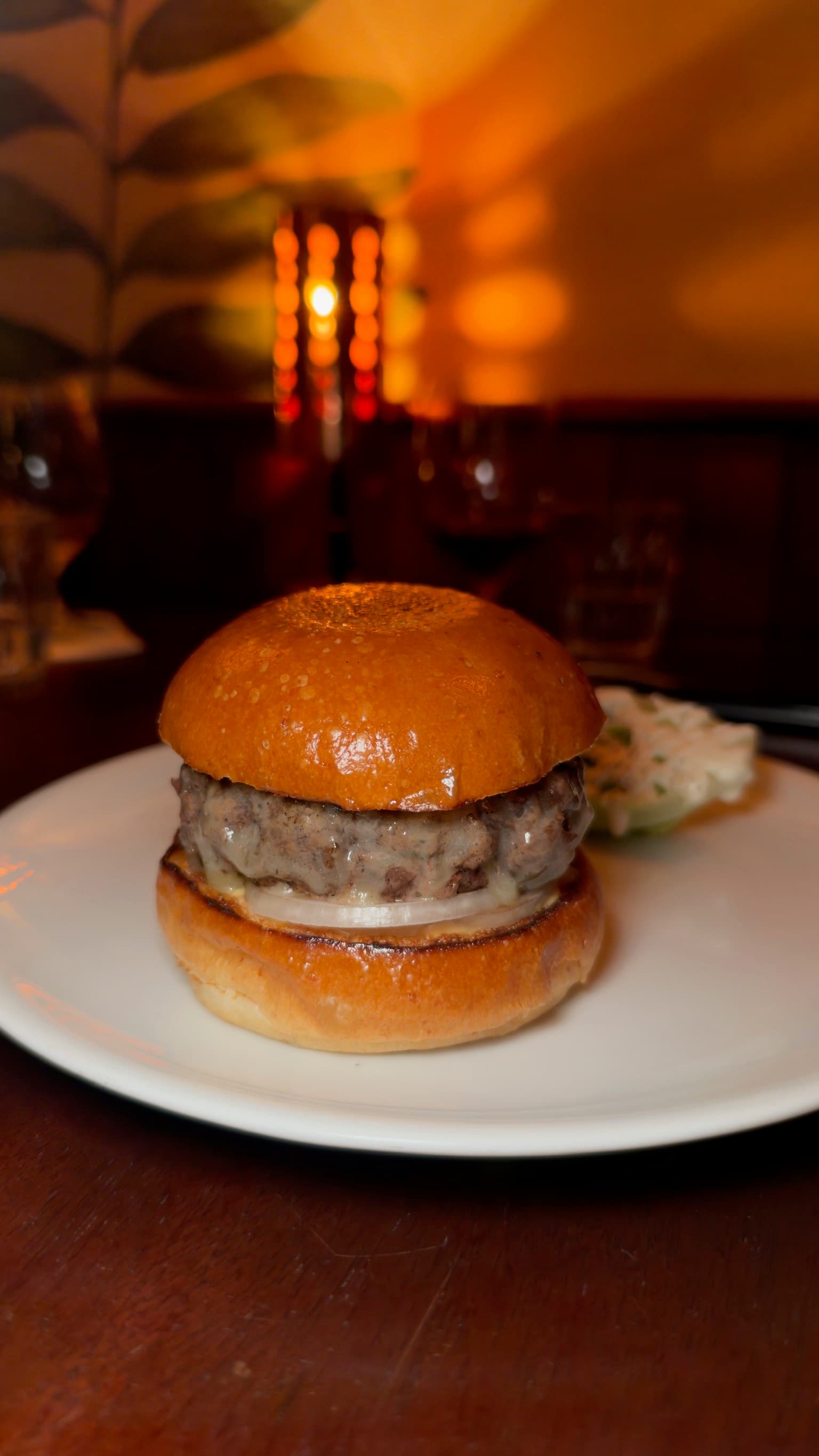 Wild Cherry's Cheeseburger in the candlelit dining room: a thick patty with melted cheese over a slice of raw onion on a glossy, toasted brioche bun, with a small salad on the side